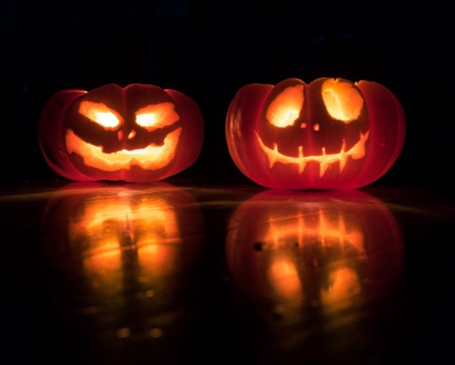 Two lit up pumpkins sitting on a table.